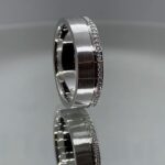 Image of a custom mens diamond wedding band placed on a reflective surface.